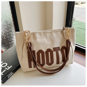 Détail du sac cabas en toile crème avec finitions en cuir marron et chaîne dorée élégante