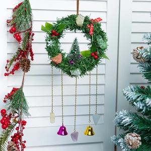 Christmas pine wreath with bells, raw stones, and a Merry Christmas ribbon on white shutters
