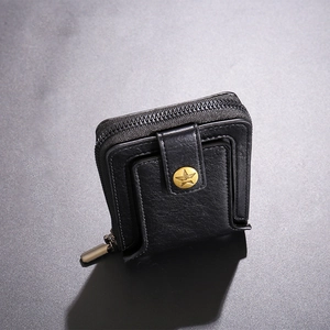 Macro shot of black pebbled leather wallet featuring a zipper and gold star snap button