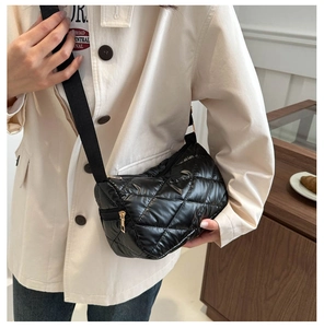 Détail d'un sac cylindrique matelassé noir avec une large bandoulière en tissu