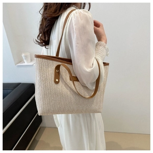 Detail of woven tote bag featuring cream body with brown leather trim and dual handles