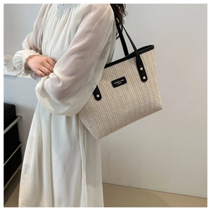Close-up of beige woven tote bag with herringbone texture and black leather straps