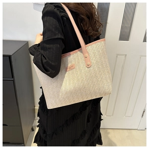 Detail of woven tote bag featuring beige V-pattern straw and pink leather handles