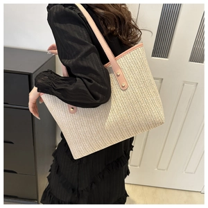 Close-up of woven straw tote bag with pink leather handles and gold rivet details
