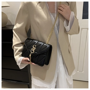 Détail d'un sac à bandoulière noir matelassé avec chaîne dorée et pendentif à pompon