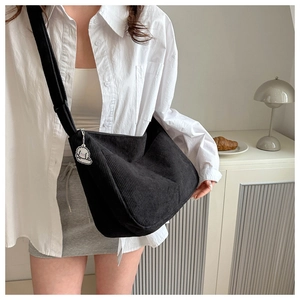 Detail of black corduroy tote bag with wide strap and cute white puppy keychain charm