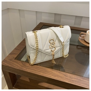 Gros plan d'un sac bandoulière blanc matelassé avec chaîne dorée et pompon décoratif