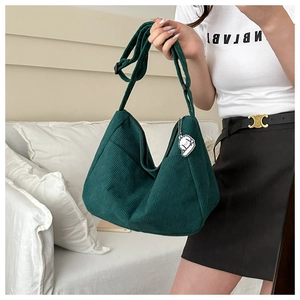 Detail of dark green corduroy hobo bag with a white cartoon dog charm and wide strap