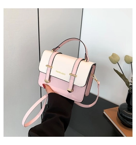 Pink and cream contrast crossbody bag with gold hardware held by hand in a chic setting