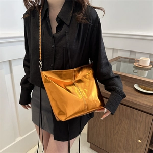 Retro metallic orange large bucket bag with chain strap worn by a model in a room