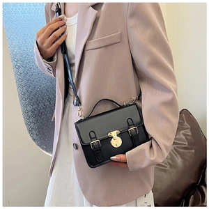 Detail of black vintage messenger bag with gold lock on a model in a lavender suit