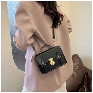 Detail of a vintage black PU messenger bag with a golden round clasp lock and metal hardware
