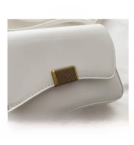 Close-up of white lychee leather texture and vintage gold metal buckle on a square bag