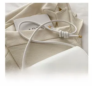 Detail of white leather shoulder bag featuring knurled metal buckle and knotted strap