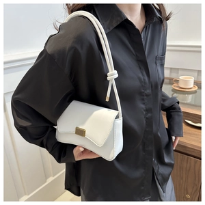 Close-up of white leather crossbody bag featuring a golden buckle and knotted shoulder strap