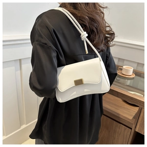 Chic white underarm bag with wavy flap and gold buckle shown on shoulder of a model