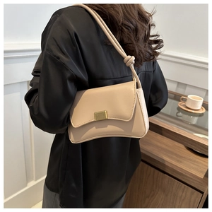 Elegant beige shoulder bag with curved base and golden clasp worn by a model