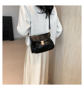 Detail of black pleated cloud bag with elegant gold circular lock on leather flap