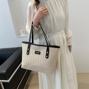 Large woven tote bag with black leather handles and minimalist brand patch