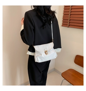 Detail view of a white leather crossbody bag with a round gold metal lock shown on a model