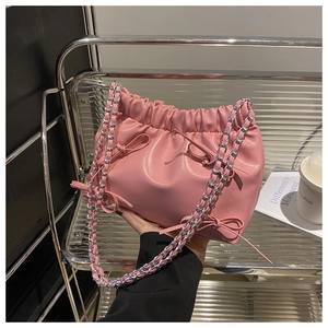Sac seau plissé rose avec nœud et bandoulière chaîne argentée tenu à la main