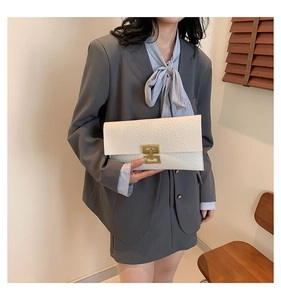 Detail of cream envelope clutch bag featuring crocodile texture and gold metal buckle