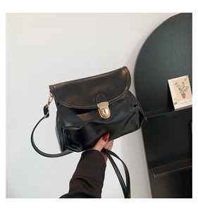 Close-up of black retro crossbody bag with glossy leather texture and gold buckle detail