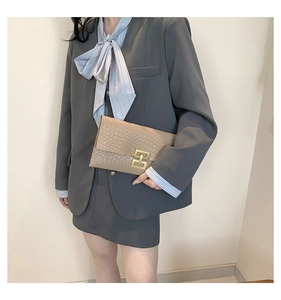 Detail of beige textured envelope clutch featuring a gold interlaced rectangular buckle