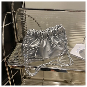 Détail d'un sac seau plissé argenté avec nœuds décoratifs et chaîne sur support moderne
