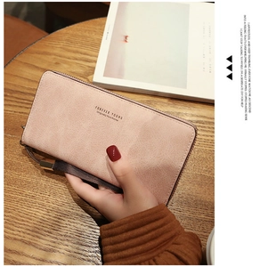 Detail of pink long leather wallet with wrist strap on a warm wooden coffee table