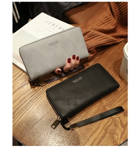 Detail of long zippered wallet with leather texture and handy wrist strap on a wooden table