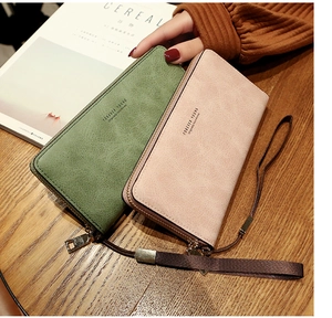Detail of long zippered wallets in matte dark green and pink on a wooden desk