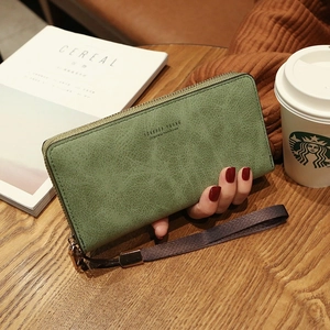 Pale green long zip-around women's clutch wallet with wrist strap on a wooden desk