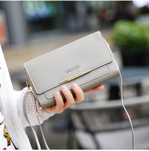 Détail de la pochette grise en cuir avec garniture dorée et tenue blanche texturée