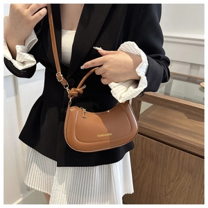 Detail of caramel crescent shoulder bag with knotted handle and embossed gold lettering