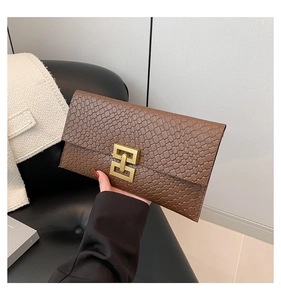 Detail showing hand holding a brown crocodile-patterned clutch with a gold buckle