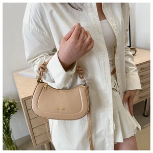 Detail of beige saddle bag with woven handle, gold lettering, and slim shoulder strap