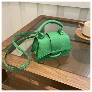 Dettaglio borsa a tracolla verde con trama a litchi su un tavolo da caffè