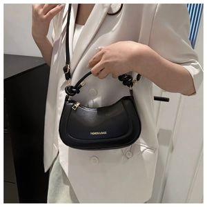 Detail of black semi-circle handbag with golden lettering and knotted handle on white blazer