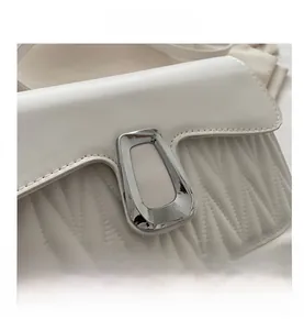 Détail d'un sac à main beige matelassé avec un fermoir géométrique en métal argenté