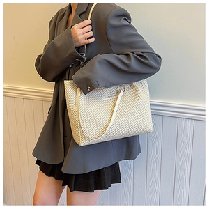 Detail of a beige woven straw tote bag with shoulder straps and Fashion label