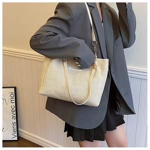 Detail of off-white straw tote showing weave texture and gold chain strap attachment