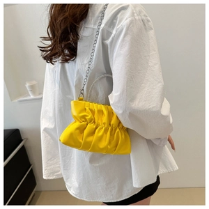 Detail van gele geplooide cloud bag met fonkelend strass handvat en zilveren ketting