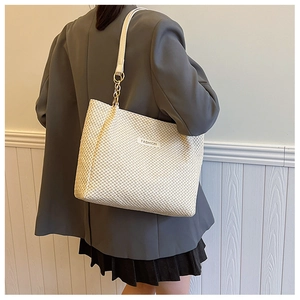Detail of white woven straw tote bag with leather strap and golden chain accents