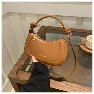 Close-up of caramel crescent handbag with knotted handle and elegant gold zipper detail