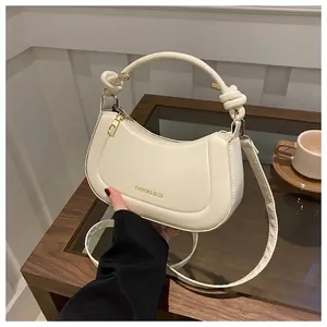 Detail of a creamy white crescent bag with knotted handle and gold zipper on a wooden table