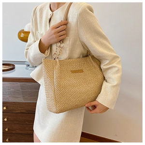 Detail of woven straw tote bag featuring leather logo tag and gold chain shoulder strap