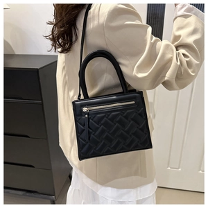 Detail of black woven leather handbag with gold hardware worn by a model in a modern room