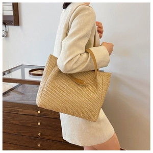 Detail view of woven straw tote bag featuring a natural herringbone texture and tan straps