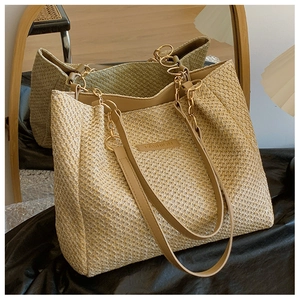 Detail of straw tote bag with leather straps and gold chains reflected on mirror surface